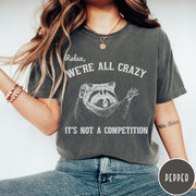 Comfort Colors tee in Pepper featuring screen print style graphic of a raccoon with text Relax We Are All Crazy