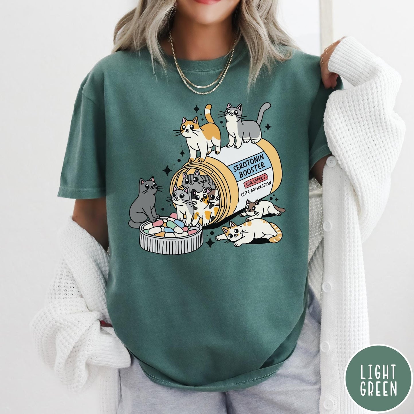 Comfort Colors tee in Light Green featuring graphic illustration of cats spilling out of a serotonin booster bottle