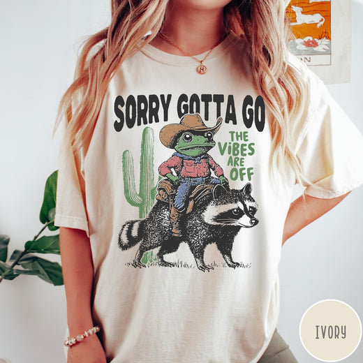 Comfort Colors tee in Ivory featuring western graphic of a cowboy frog riding a raccoon with cactus