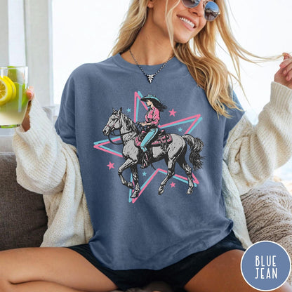 Comfort Colors tee in Blue Jean featuring retro cowgirl graphic with a woman riding a horse inside a star