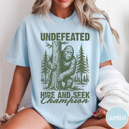 Comfort Colors tee in Chambray featuring vintage style Bigfoot graphic hiding behind a tree in the forest