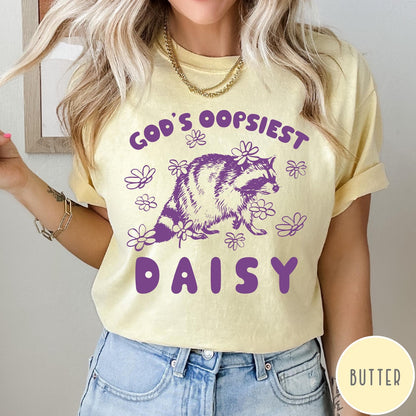 Comfort Colors tee in Butter featuring whimsical raccoon graphic with daisy flowers and God's Oopsiest Daisy text