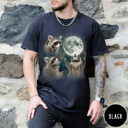 Comfort Colors tee in Black featuring artistic graphic of three raccoons reaching toward a bright full moon