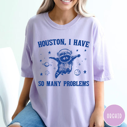 Comfort Colors tee in Orchid featuring space style graphic of a raccoon wearing an astronaut helmet floating