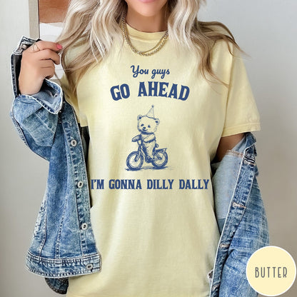 Comfort Colors tee in Butter featuring illustration style graphic of a bear wearing a party hat riding bicycle
