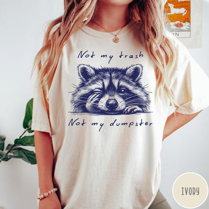 Comfort Colors tee in Ivory featuring illustrated style graphic of a winking raccoon with text not my trash