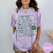 Comfort Colors tee in Orchid featuring retro camping adventure collage graphic with tent, campfire, and outdoor icons