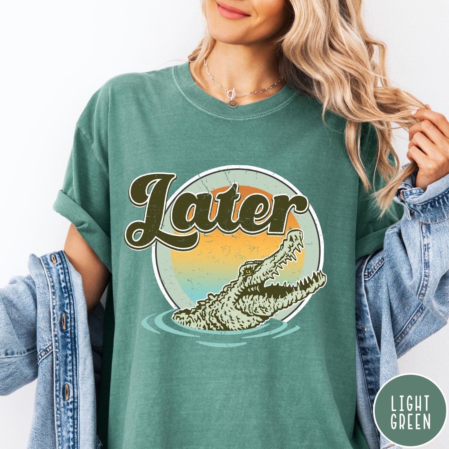 Comfort Colors tee in Light Green featuring vintage style graphic of an alligator emerging from water with sunset background