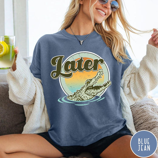Comfort Colors tee in Blue Jean featuring vintage style graphic of an alligator emerging from water with sunset background