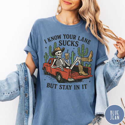 Comfort Colors tee in Blue Jean featuring western skeleton graphic with cowboy hat and boots in pickup truck
