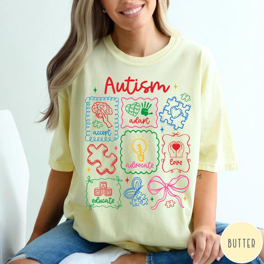 Comfort Colors tee in Butter featuring coquette style autism awareness graphic with puzzle pieces and colorful icons