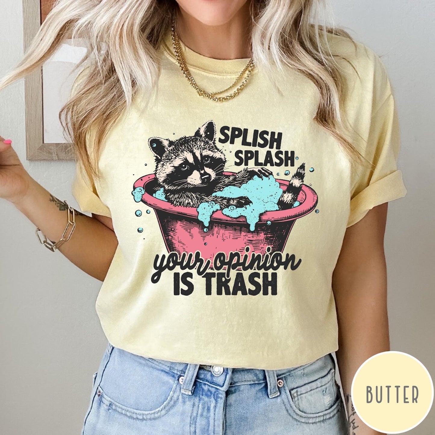 Comfort Colors tee in Butter featuring illustrative graphic of a raccoon sitting in a pink bathtub