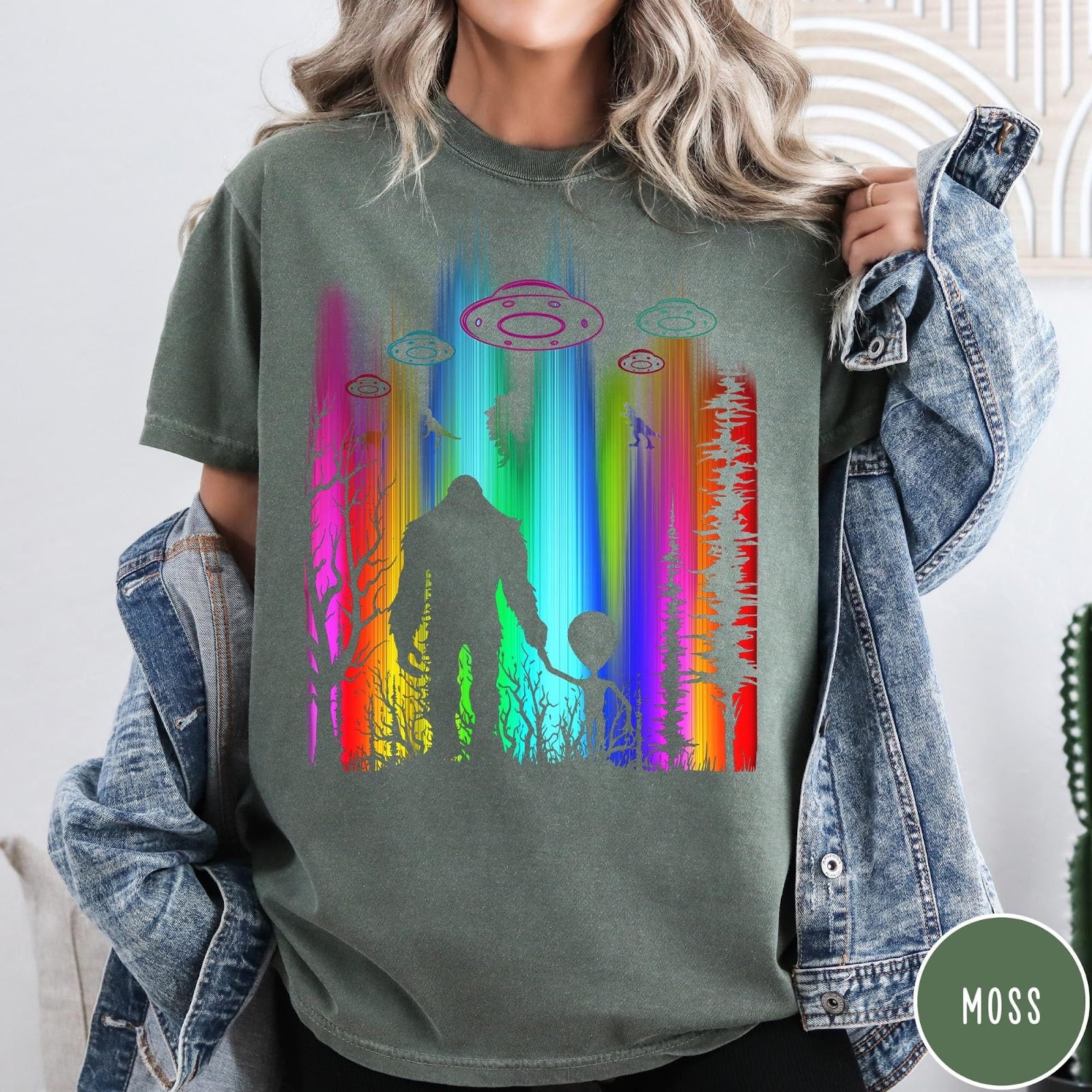 Comfort Colors tee in Moss featuring a vibrant graphic of Bigfoot and an alien holding hands in forest