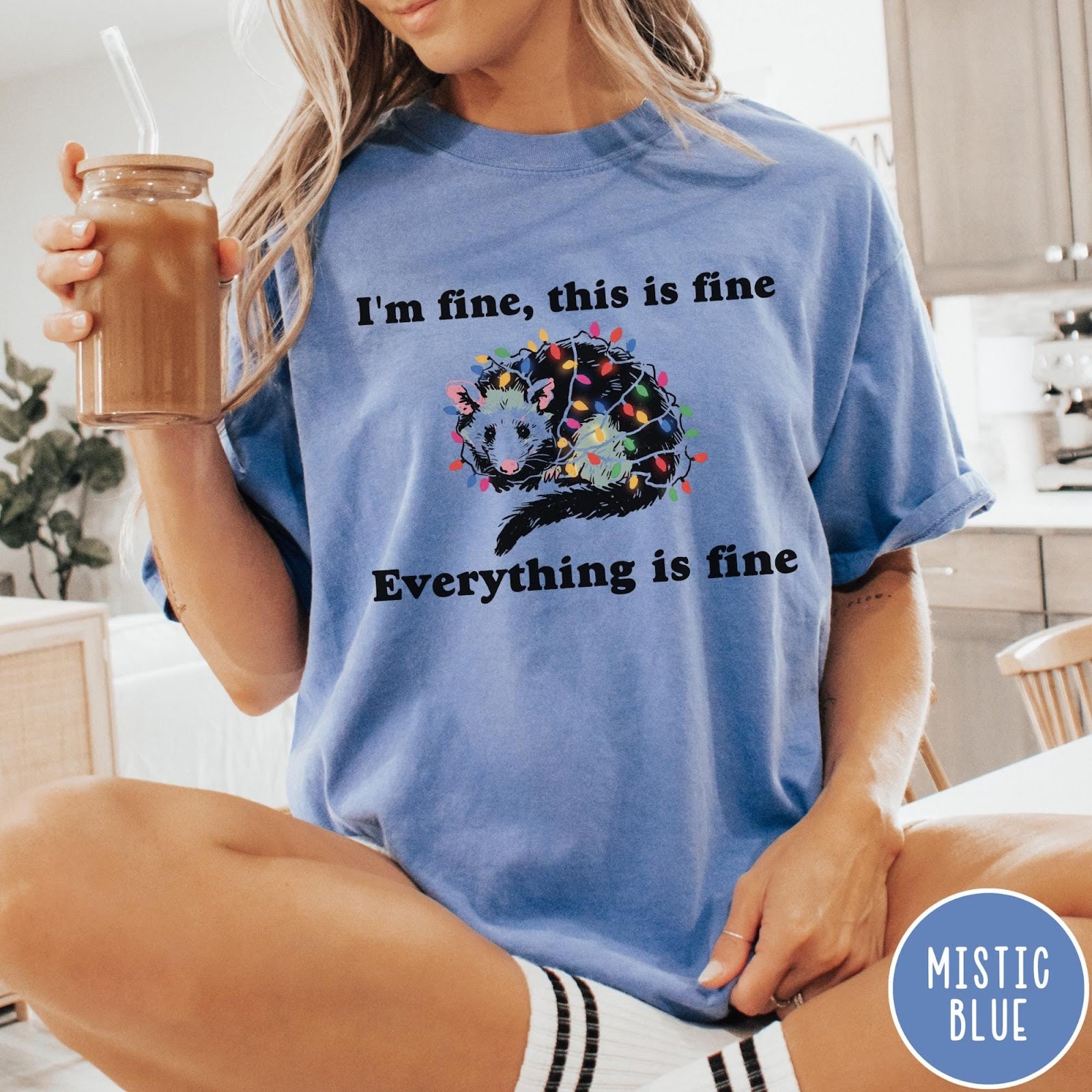 Comfort Colors tee in Mistic Blue featuring graphic illustration of an opossum tangled in colorful Christmas lights
