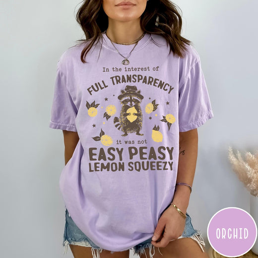 Comfort Colors tee in Orchid featuring graphic illustration of a raccoon wearing a hat holding a lemon