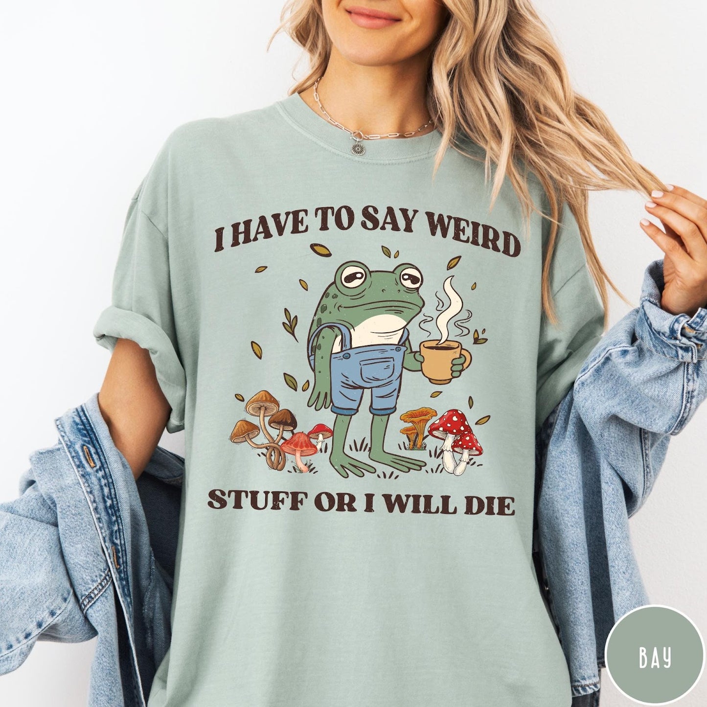 Comfort Colors tee in Bay featuring cartoon style frog wearing overalls holding a coffee mug with mushrooms