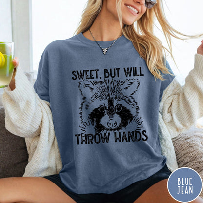 Comfort Colors tee in Blue Jean featuring graphic style raccoon illustration with text Sweet But Will Throw Hands