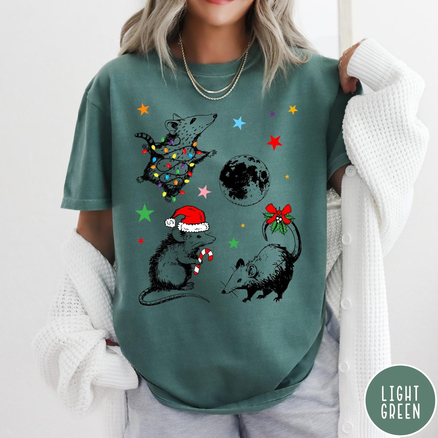 Comfort Colors tee in Light Green featuring holiday possum graphic with Christmas lights, candy cane, and moon.