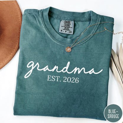 Comfort Colors tee in Blue Spruce featuring script design Grandma Est. 2026 announcement graphic in white
