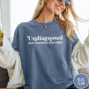 Comfort Colors tee in Blue Jean featuring mental health humor text that reads Undiagnosed but somethin aint right