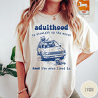 Comfort Colors tee in Ivory featuring illustrated style graphic of raccoons sitting in and around a car