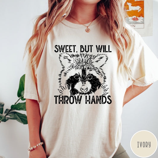 Comfort Colors tee in Ivory featuring graphic style raccoon illustration with text Sweet But Will Throw Hands