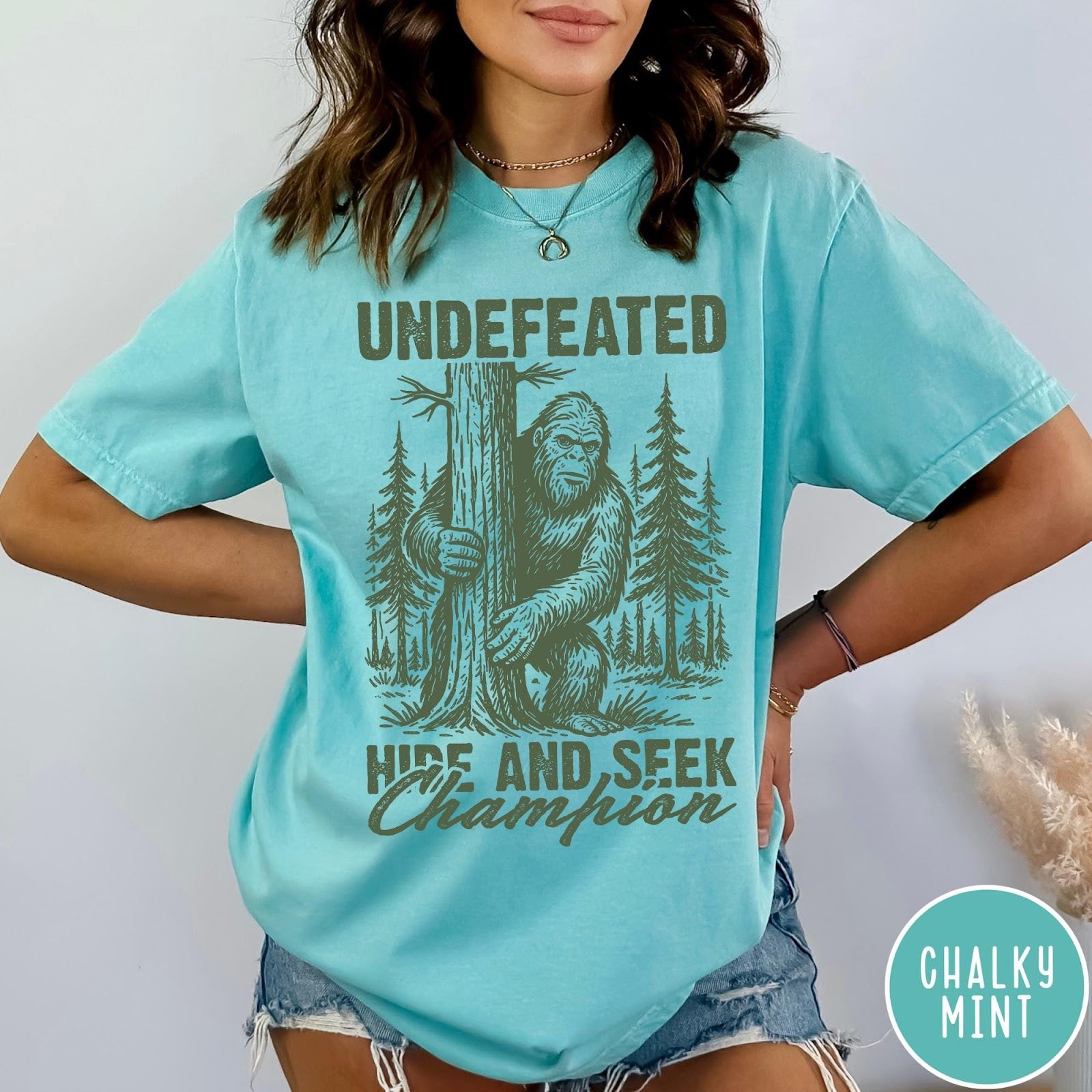 Comfort Colors tee in Chalky Mint featuring vintage style graphic of Bigfoot hiding behind a large pine tree