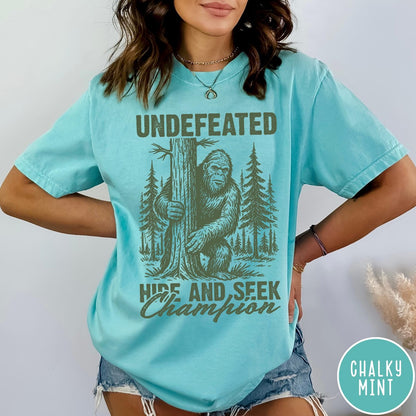 Comfort Colors tee in Chalky Mint featuring vintage style graphic of Bigfoot hiding behind a large pine tree