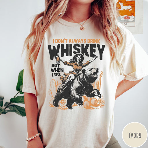 Comfort Colors tee in Ivory featuring vintage style graphic of a woman riding a bear holding whiskey