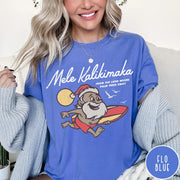 Comfort Colors tee in Flo Blue featuring vintage style graphic of a surfing Santa Claus on vacation