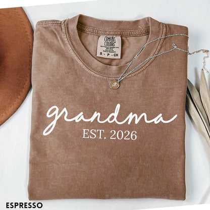 Comfort Colors tee in Espresso featuring cursive Grandma Est 2026 text in a clean white graphic style