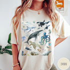 Comfort Colors tee in Ivory featuring watercolor style graphic of various ocean animals including whales and sharks