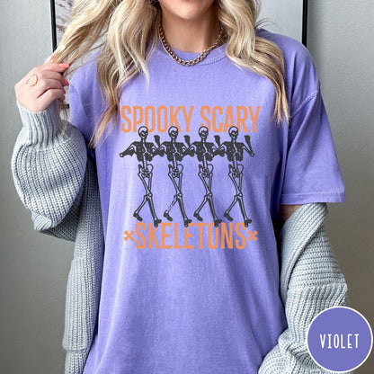 Comfort Colors tee in Violet featuring dancing skeletons graphic with Spooky Scary Skeletons text in orange