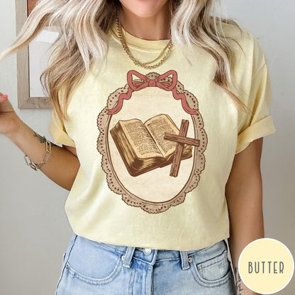 Comfort Colors tee in Butter featuring vintage style graphic of an open Bible and wooden Christian cross.