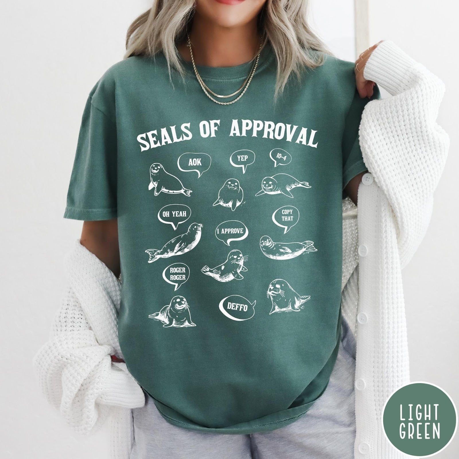 Comfort Colors tee in Light Green featuring illustrative style graphic with multiple seals and speech bubbles saying approval phrases
