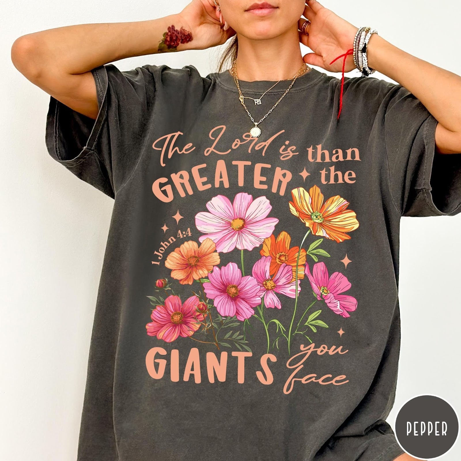 Comfort Colors tee in Pepper featuring floral Bible verse graphic design with 1 John 4:4 scripture text