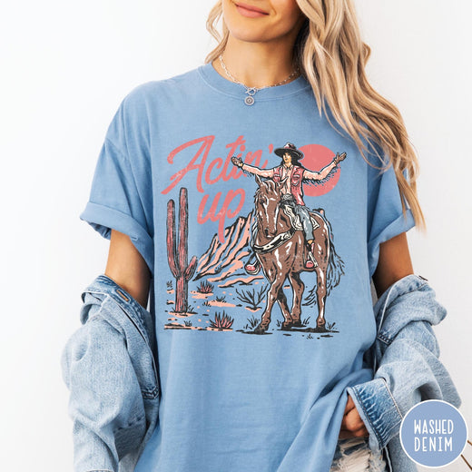 Comfort Colors tee in Washed Denim featuring western style graphic of a cowgirl riding a horse in the desert