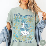 Comfort Colors tee in Bay featuring whimsical graphic style with a goose wearing a bonnet and floral border