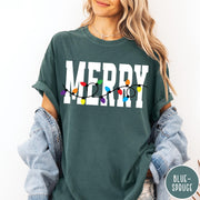 Comfort Colors tee in Blue Spruce featuring holiday style graphic with white Merry text and colorful Christmas lights