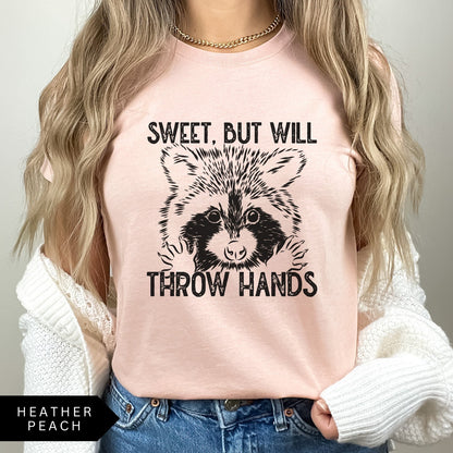 Comfort Colors tee in Heather Peach featuring graphic style raccoon illustration with text Sweet, but will throw hands