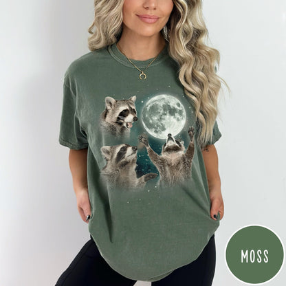 Comfort Colors tee in Moss featuring artistic graphic of three raccoons reaching toward a bright full moon