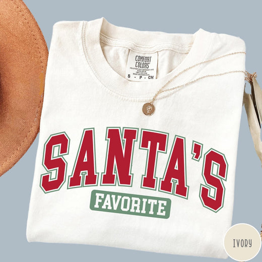 Comfort Colors tee in Ivory featuring collegiate style Santa's Favorite Christmas graphic with red and green text