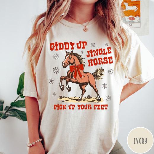 Comfort Colors tee in Ivory featuring festive holiday graphic with a prancing horse wearing a red bow