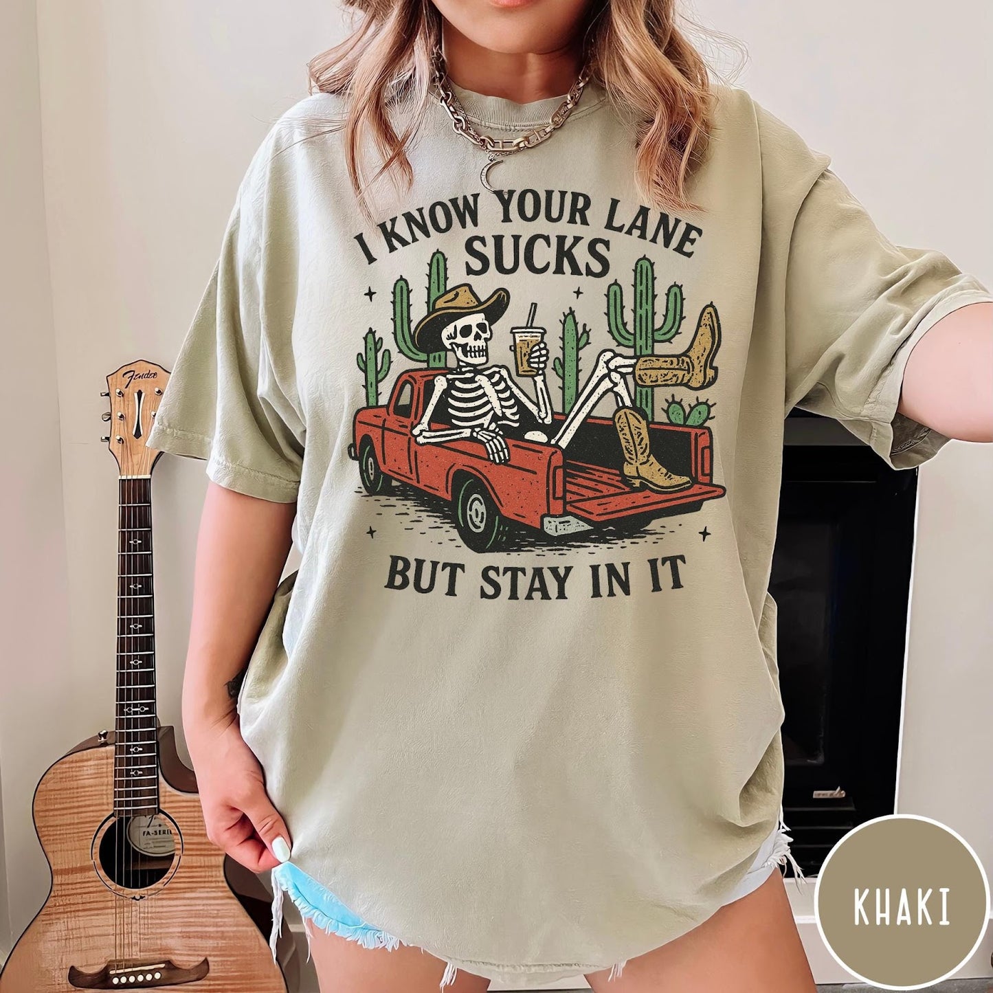 Comfort Colors tee in Khaki featuring western skeleton graphic with cowboy hat and boots in pickup truck