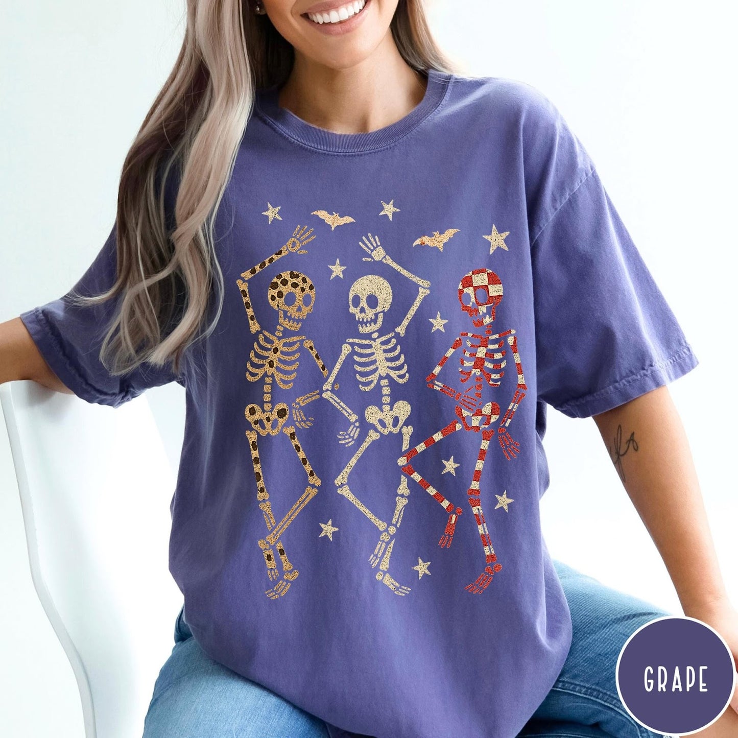 Comfort Colors tee in Grape featuring dancing skeletons design with three skeletons, stars, and bats graphic