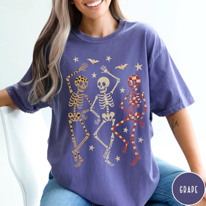 Comfort Colors tee in Grape featuring dancing skeletons design with three skeletons, stars, and bats graphic