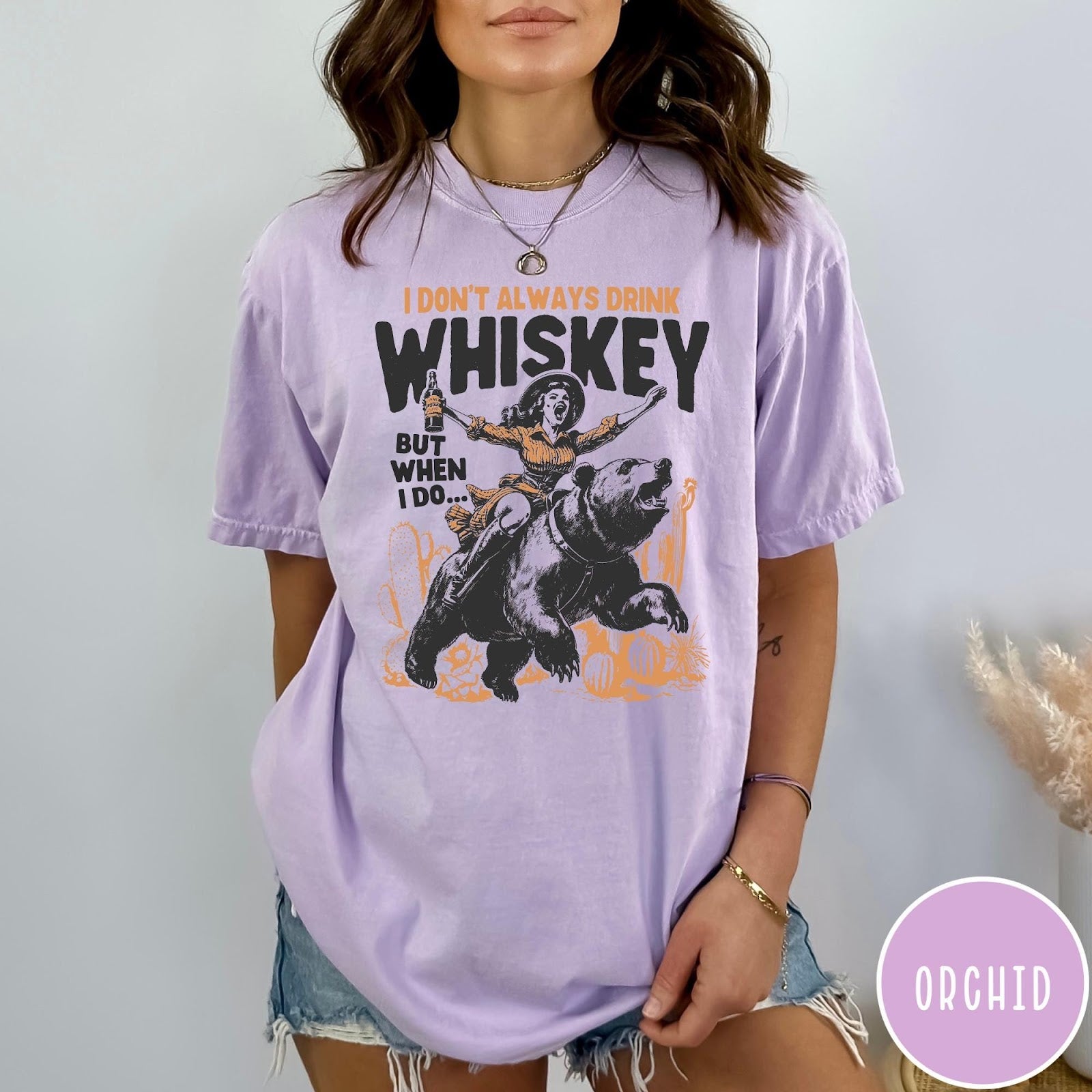 Comfort Colors tee in Orchid featuring vintage style graphic of a woman riding a bear holding whiskey