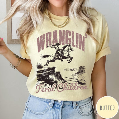 Comfort Colors tee in Butter featuring western style graphic of a cowboy on horseback jumping a canyon