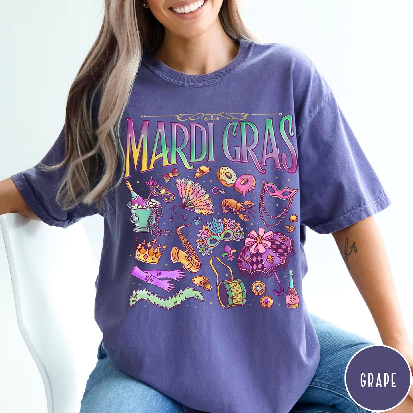 Comfort Colors tee in Grape featuring vintage style Mardi Gras icons including a saxophone, mask, and umbrella.