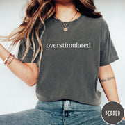 Comfort Colors tee in Pepper featuring typography design with the word overstimulated printed in white text